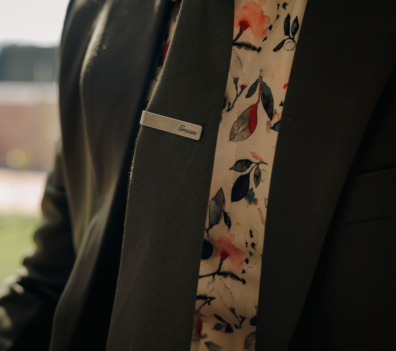 Close-up of groom's dark suit lapel with floral tie and silver tie bar.
