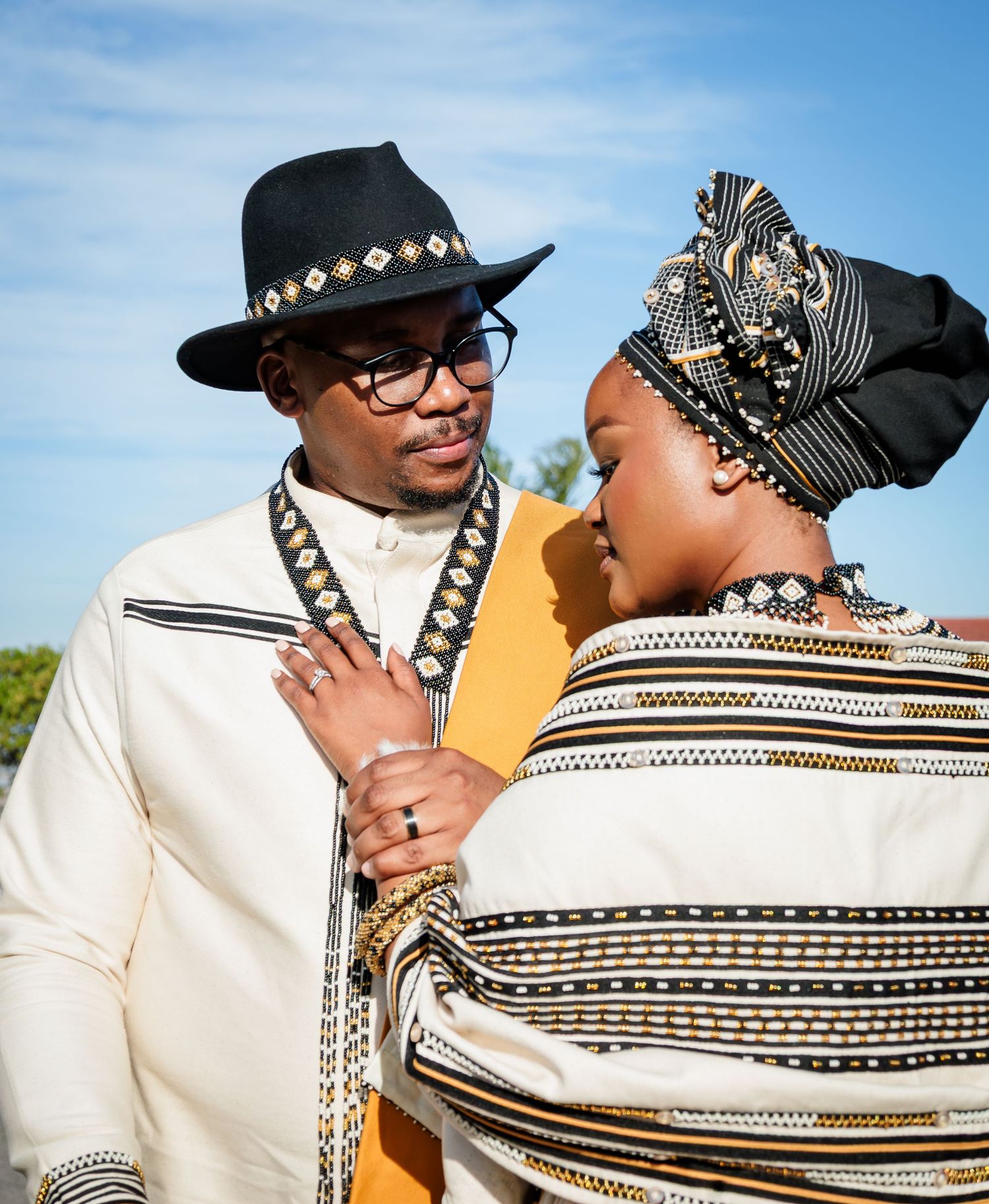 Couple in traditional Xhosa attire with black, white, and gold patterns, sharing an intimate moment outdoors.