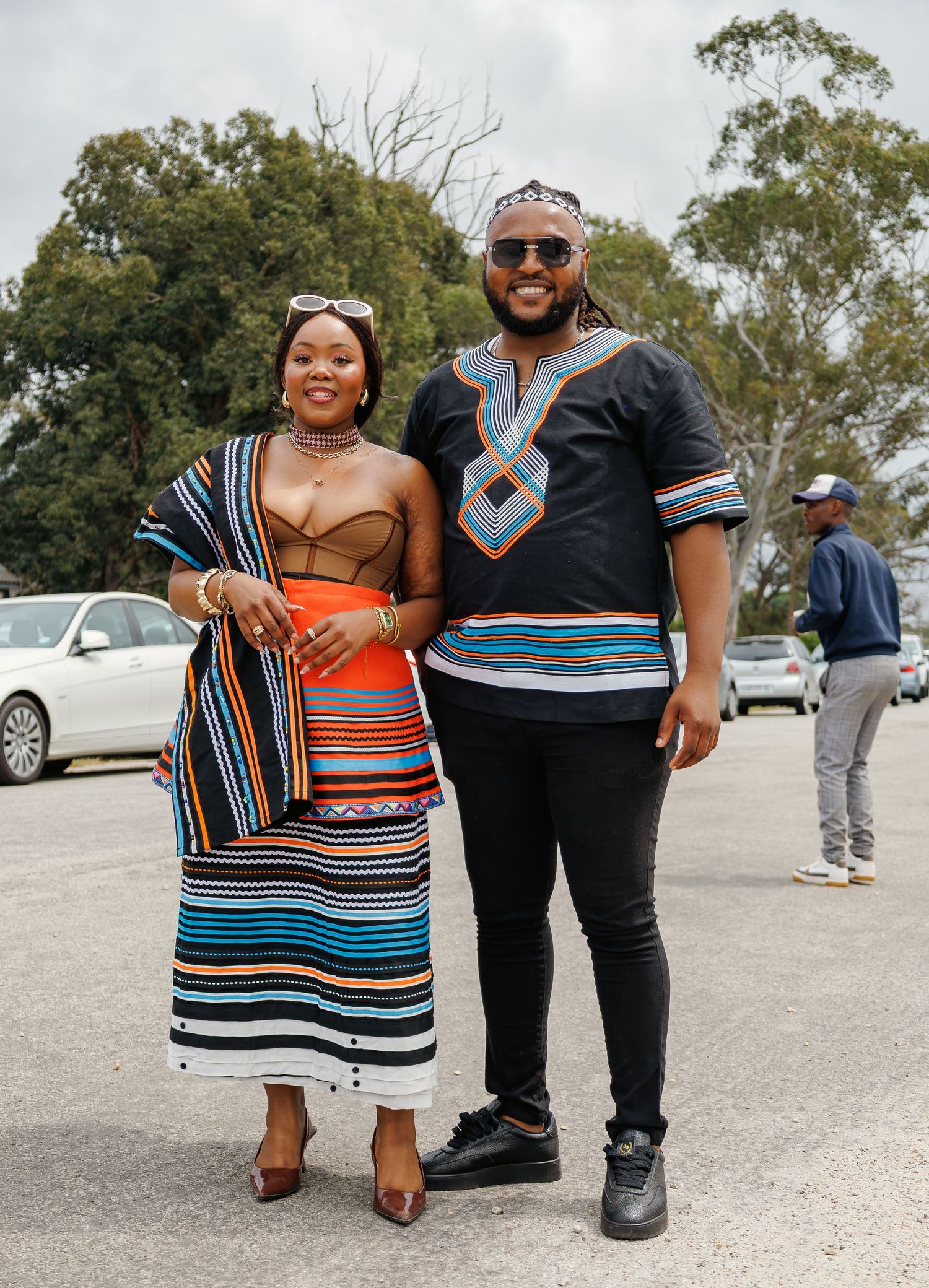 A couple poses outdoors wearing matching Xhosa-inspired striped traditional South African clothing.