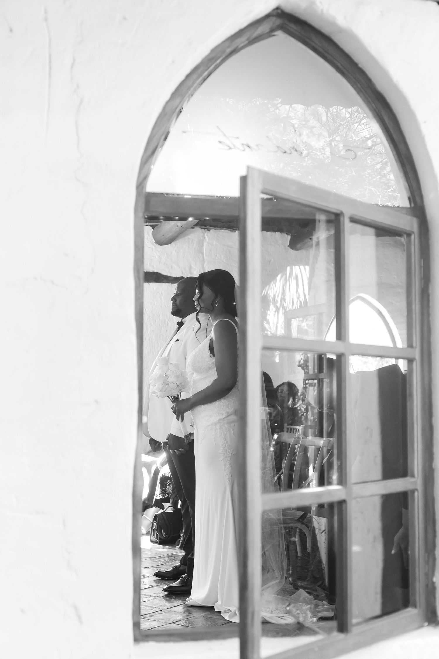 Black and white image of a bride and groom standing inside a chapel arched window.