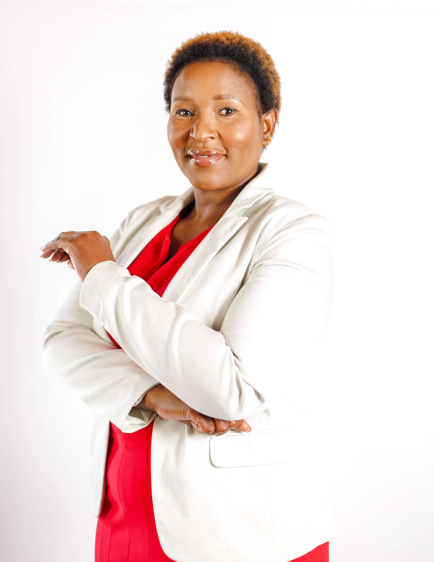 Professional woman in white blazer and red dress posing with arms crossed against white background.