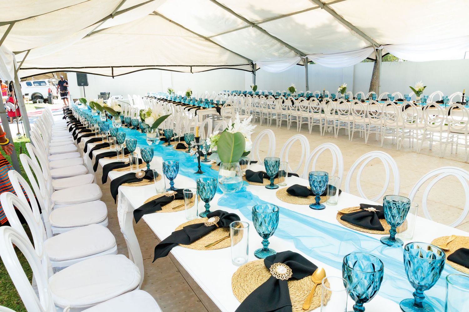 Elegant event tent with long tables set with turquoise glasses and black napkins.