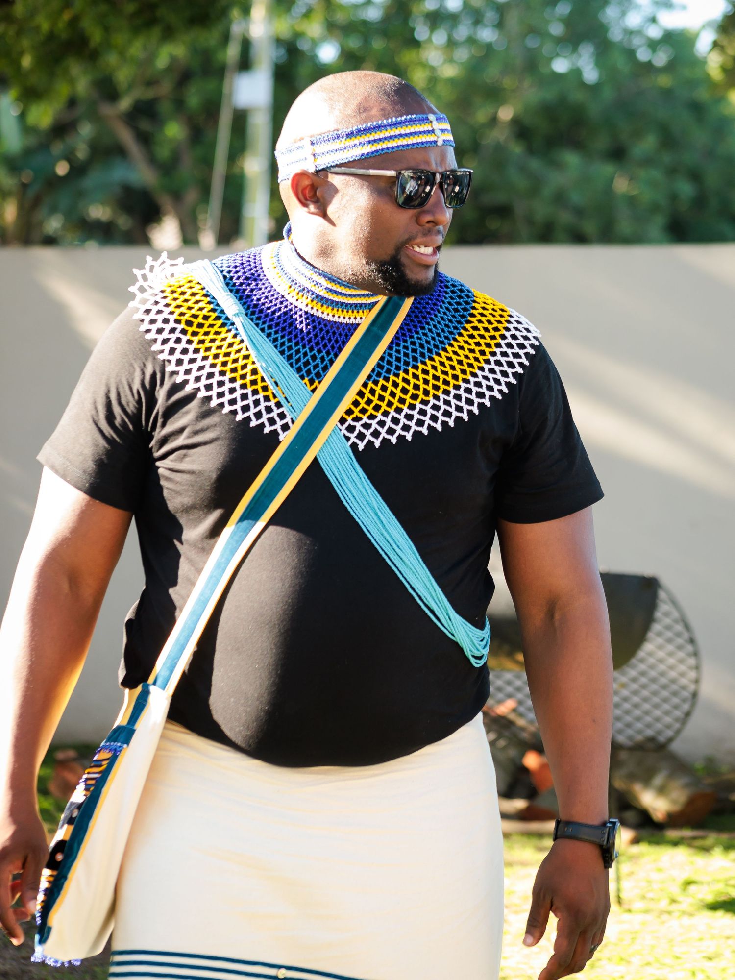 Man in vibrant Zulu beaded necklace and traditional attire at an outdoor cultural event.