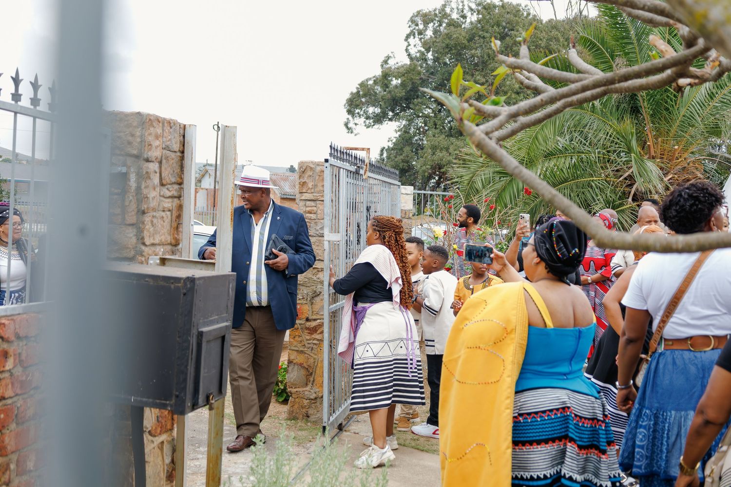 Man in white hat addresses diverse crowd outdoors at a traditional African cultural event.