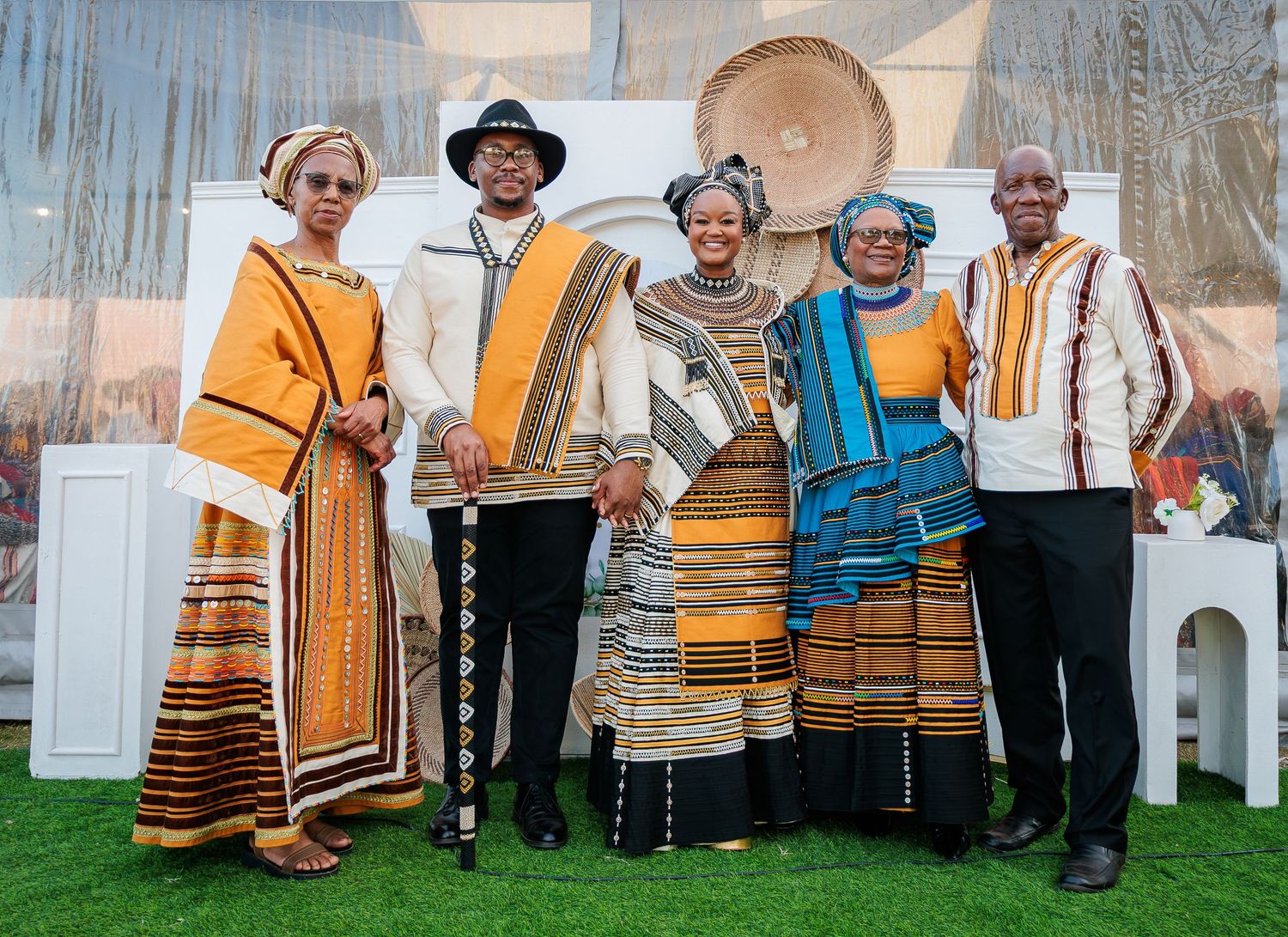 Family of five posing in vibrant traditional Xhosa attire at a formal cultural celebration indoors.