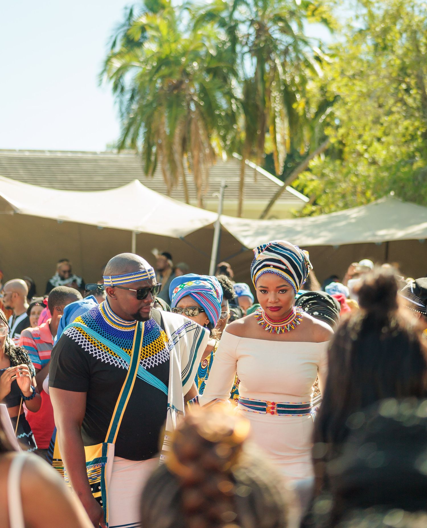 Couple in traditional Zulu and Xhosa attire walking through guests at an outdoor wedding.