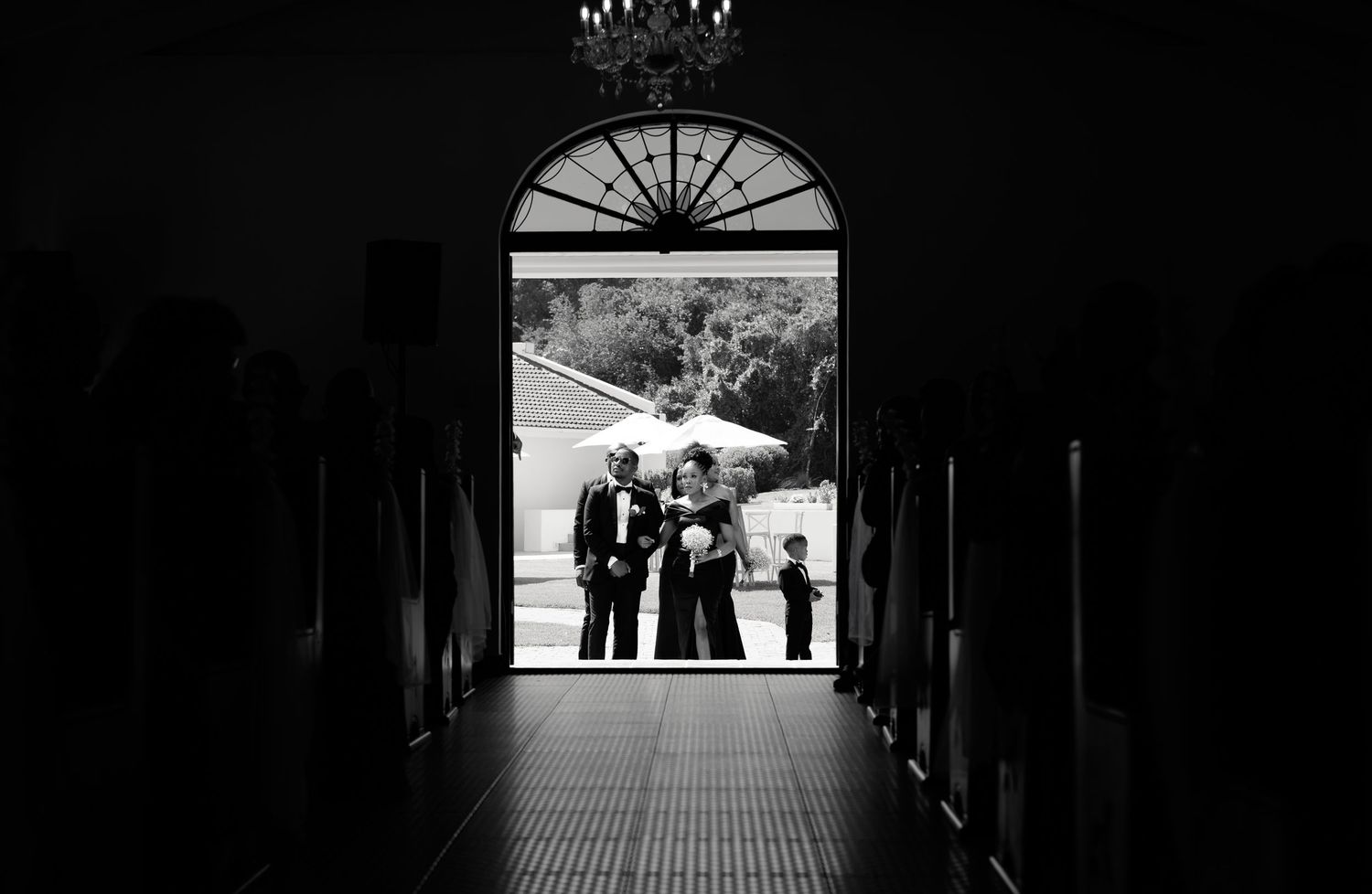 Silhouette of wedding party standing in arched church doorway, black and white photography.