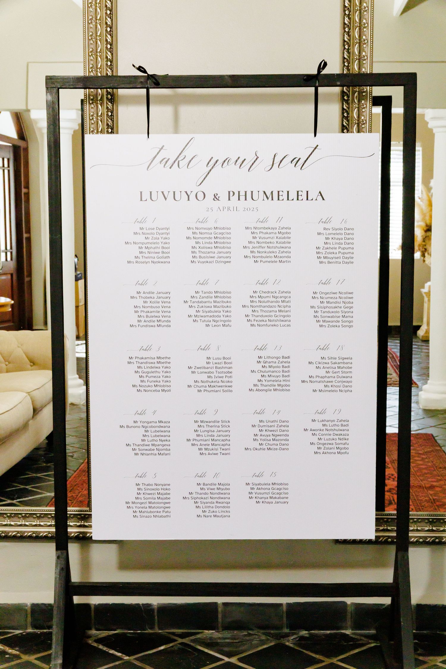 Elegant wedding seating chart for Luvuyo and Phumelela displayed on black easel in venue.