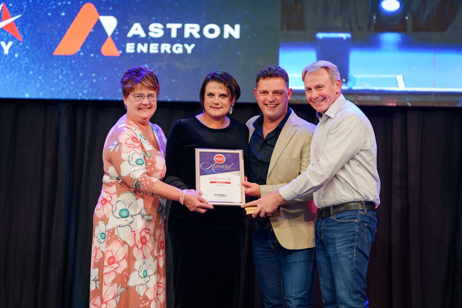 Four people proudly display certificate award on stage at Astron Energy corporate event.