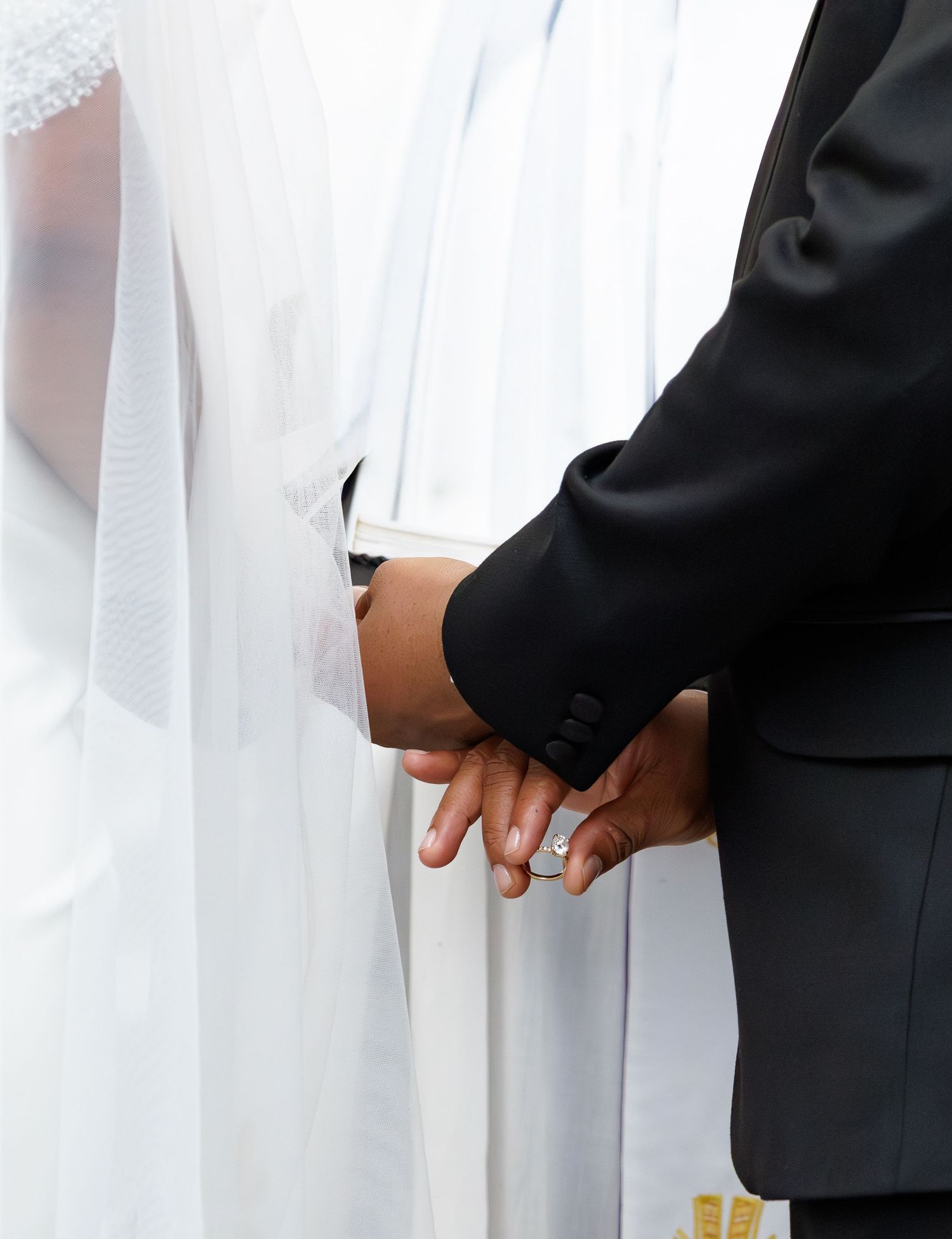 Close-up of bride and groom holding hands during wedding ceremony showing rings.