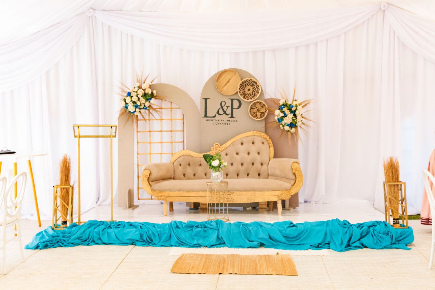 Elegant wedding sweetheart table with gold loveseat, teal fabric, and floral arrangements under white draping.