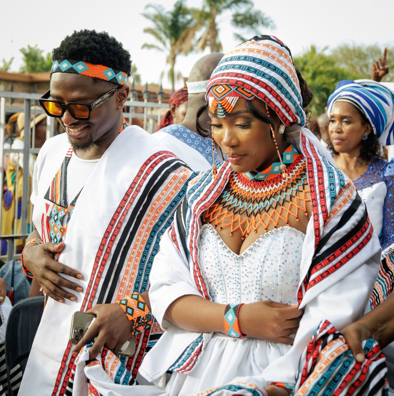 Couple in traditional African attire with colorful beadwork and white garments at a cultural ceremony.
