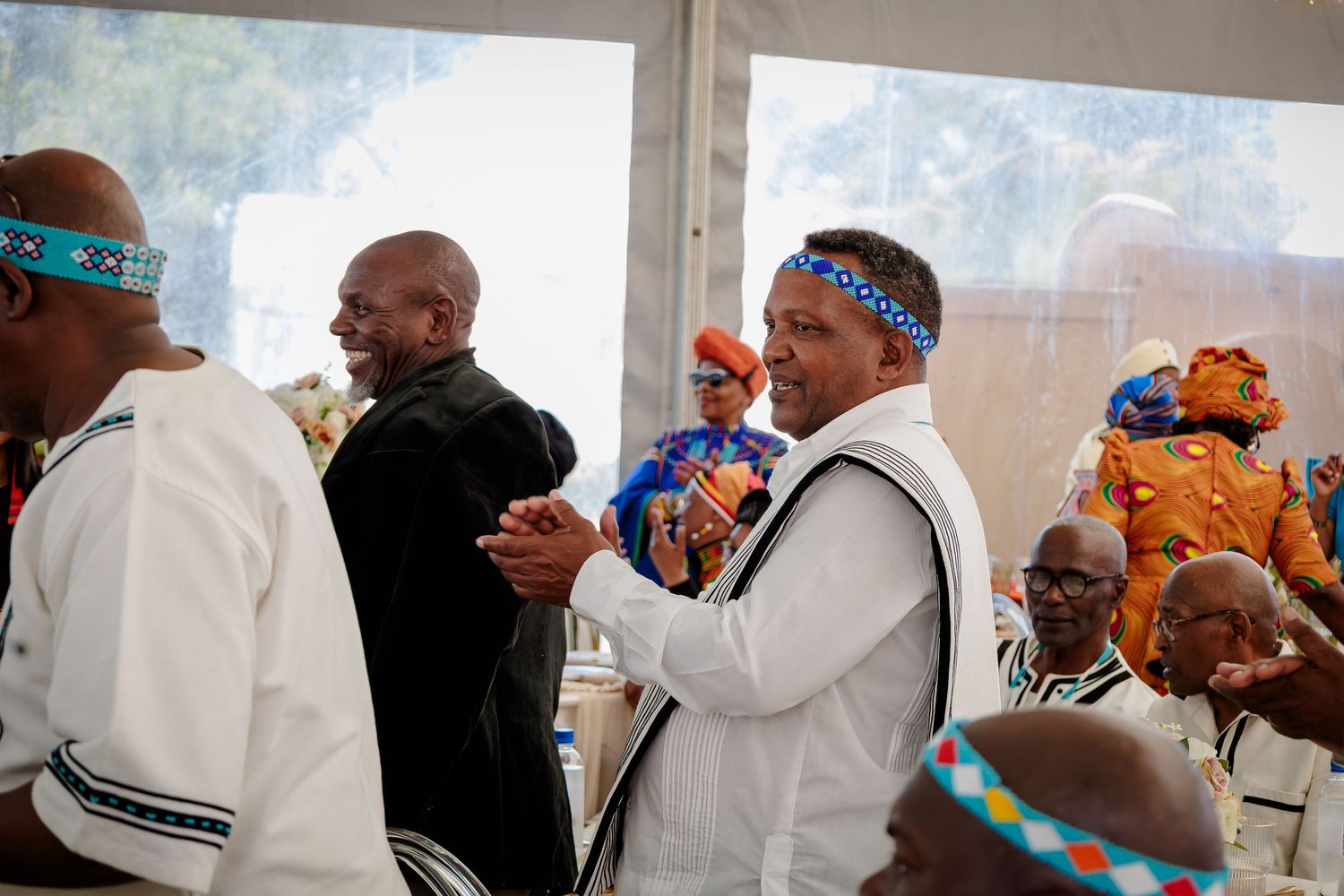 Men in traditional Xhosa attire with beaded headbands celebrating at a cultural wedding.