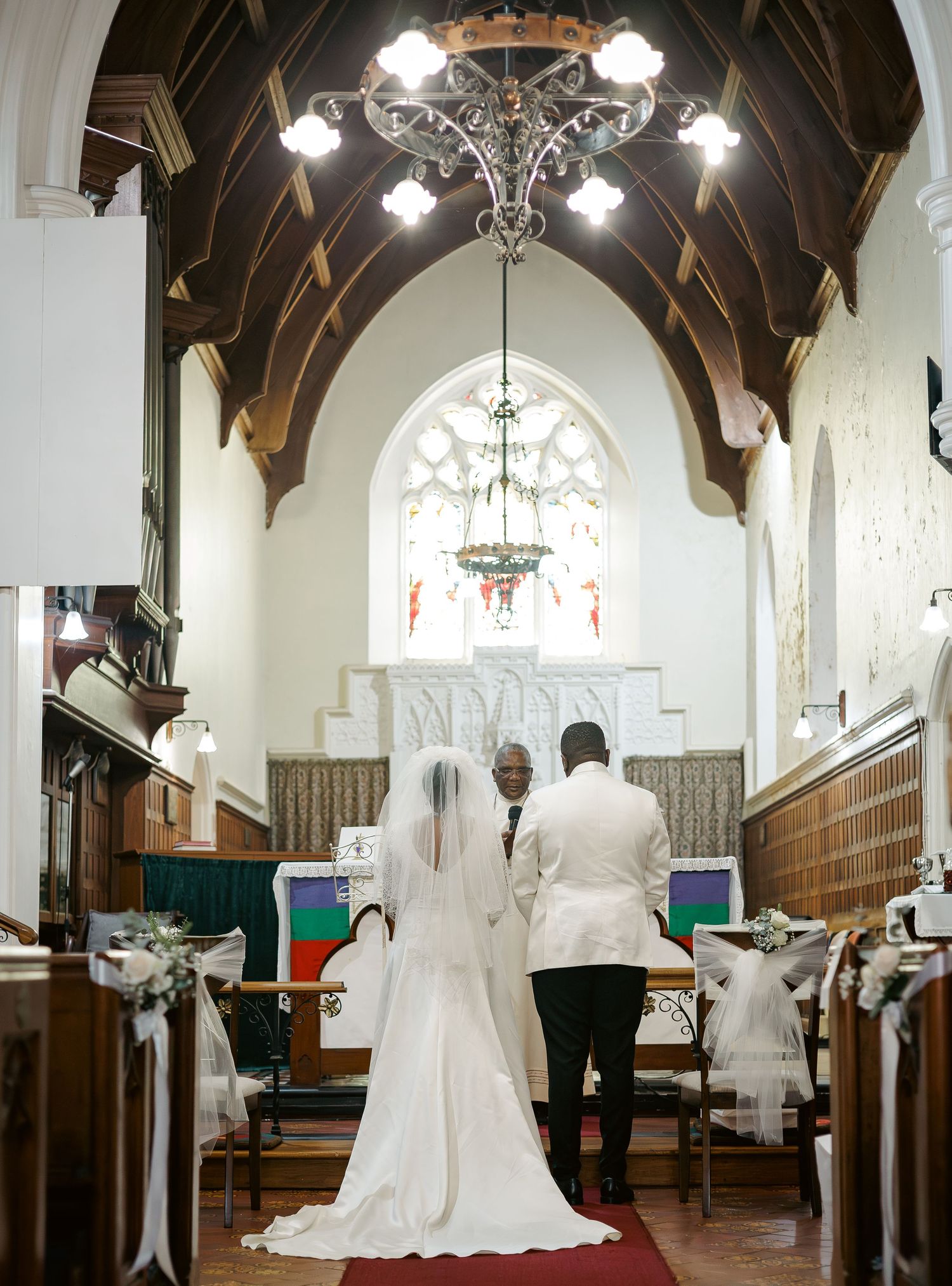 Bride and groom stand at church altar during wedding ceremony beneath ornate chandelier.