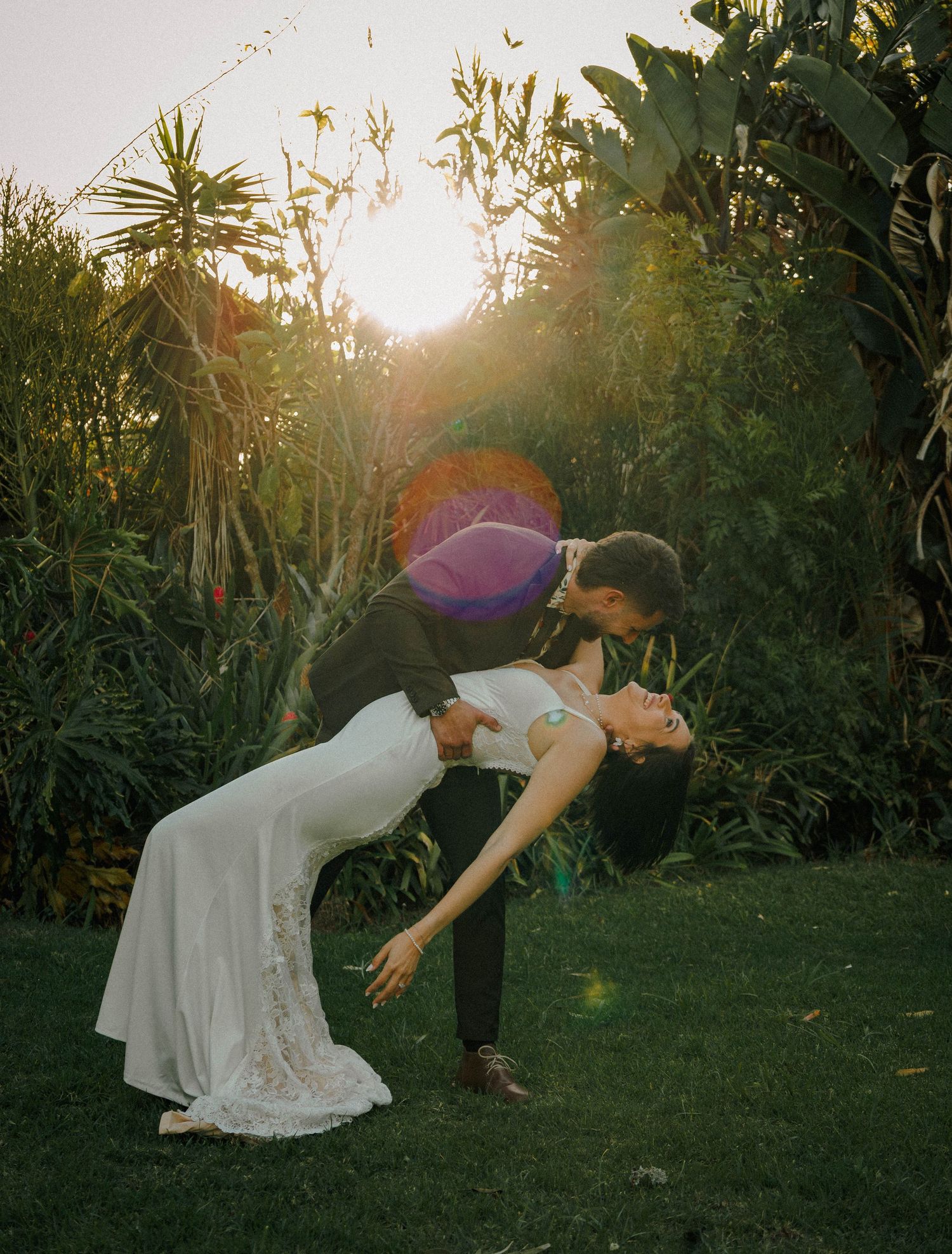 Couple sharing a romantic dip kiss in a lush garden at golden hour sunset.