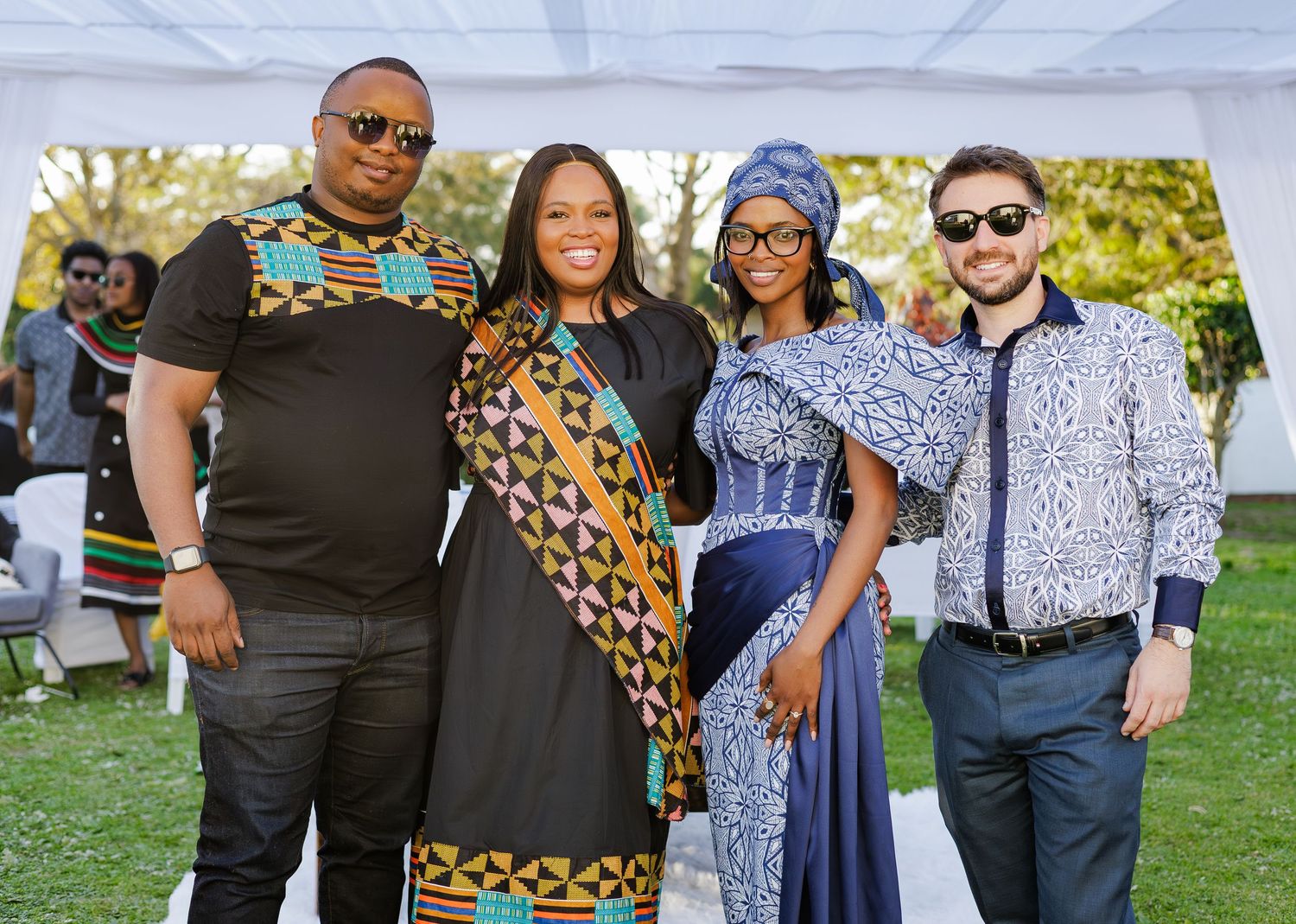 Four people posing together at an African traditional celebration wearing colorful Kente and Ndebele cultural attire outdoors.
