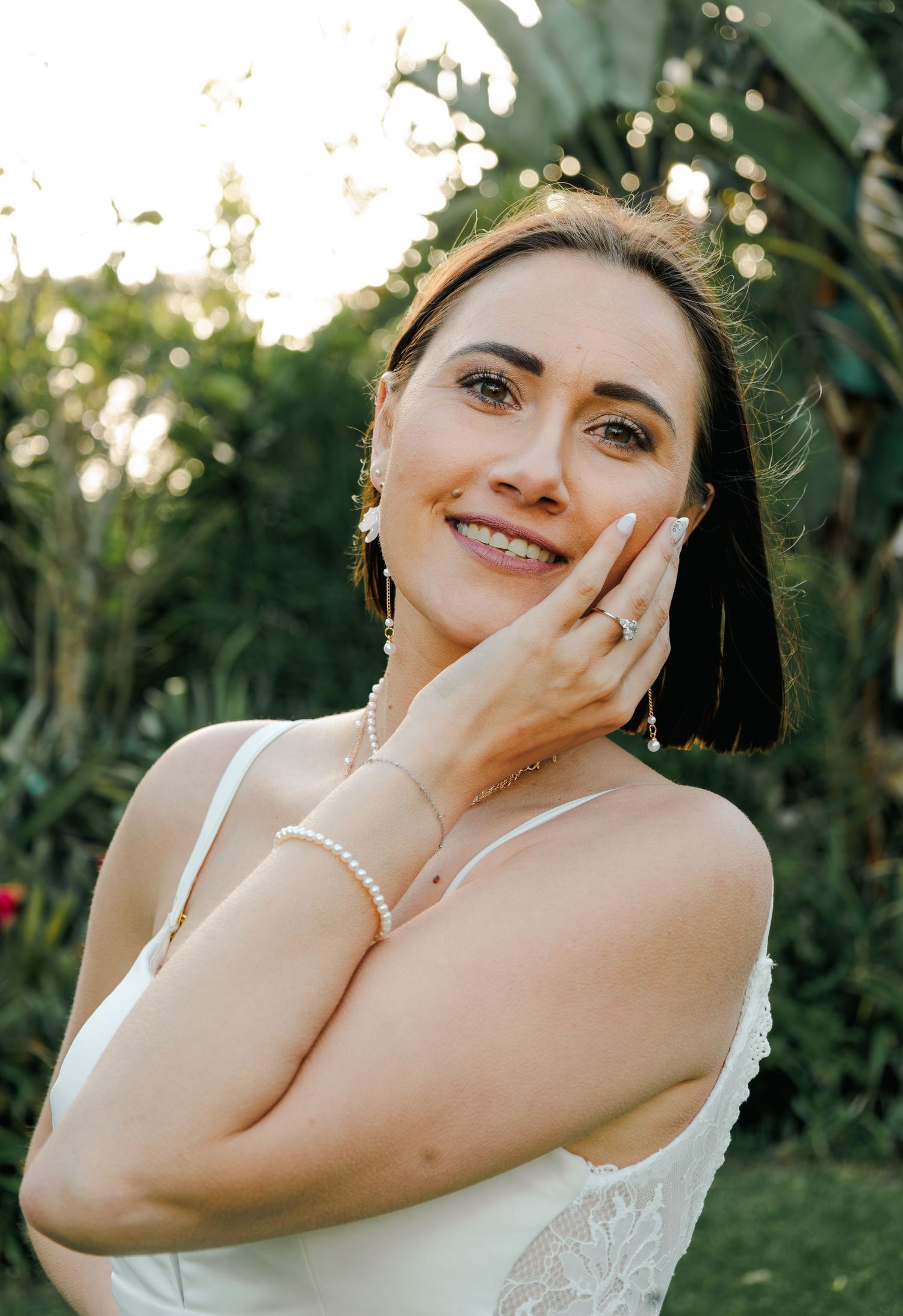 Elegant bride with pearl bracelet and diamond ring smiling softly in garden.