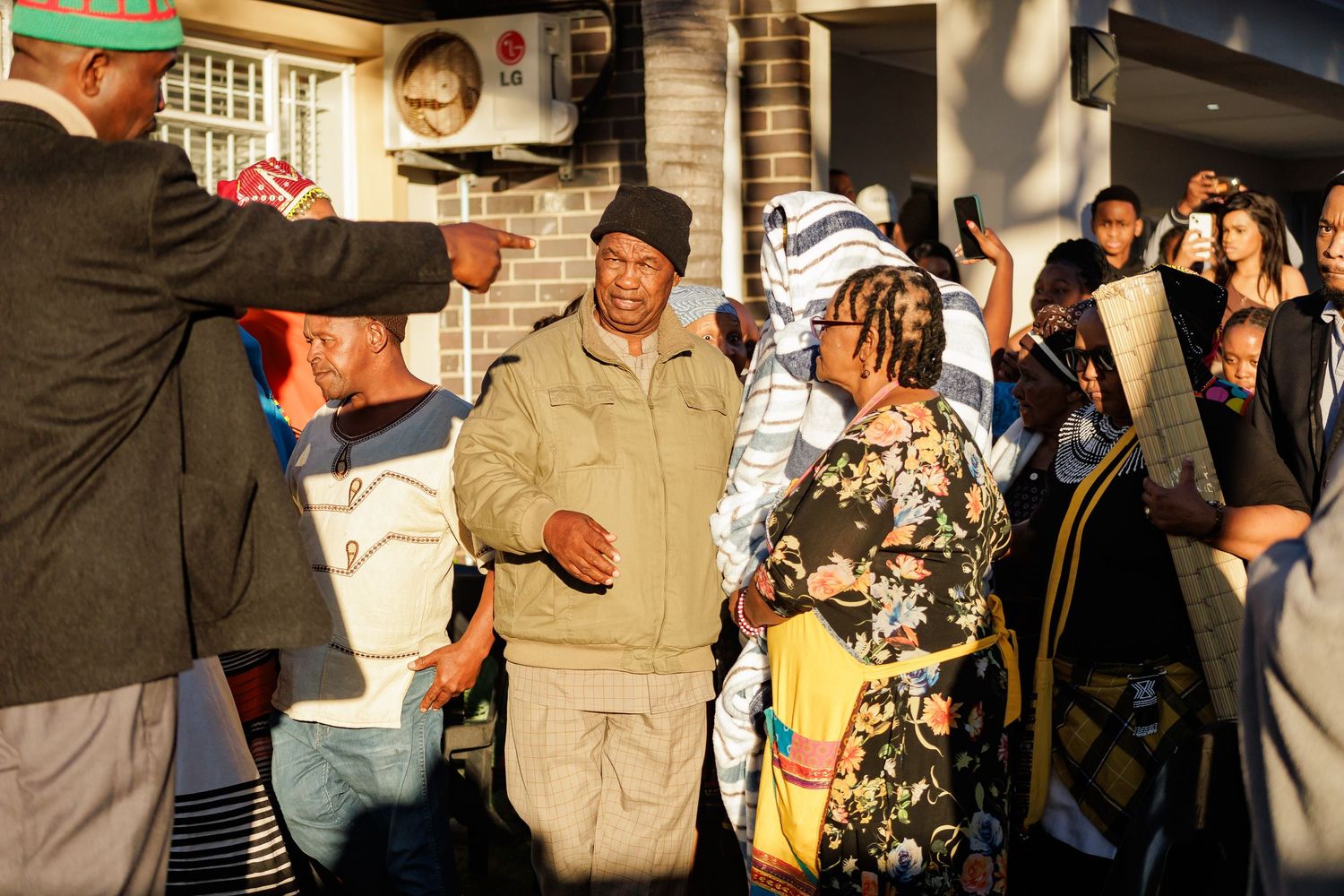 People in traditional African clothing gather outside a home during a cultural ceremony.