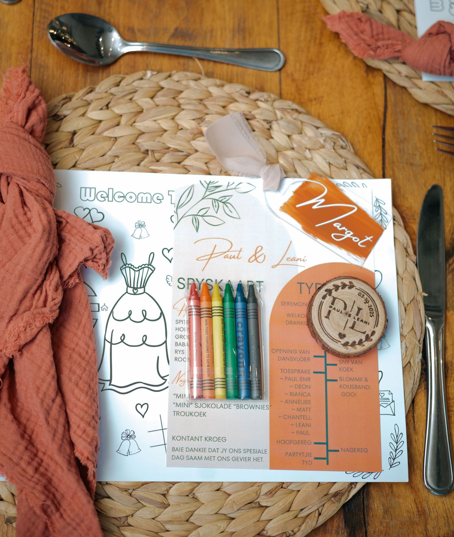 Children's wedding activity kit with crayons, coloring page, menu card, and personalized name tag on a woven placemat.