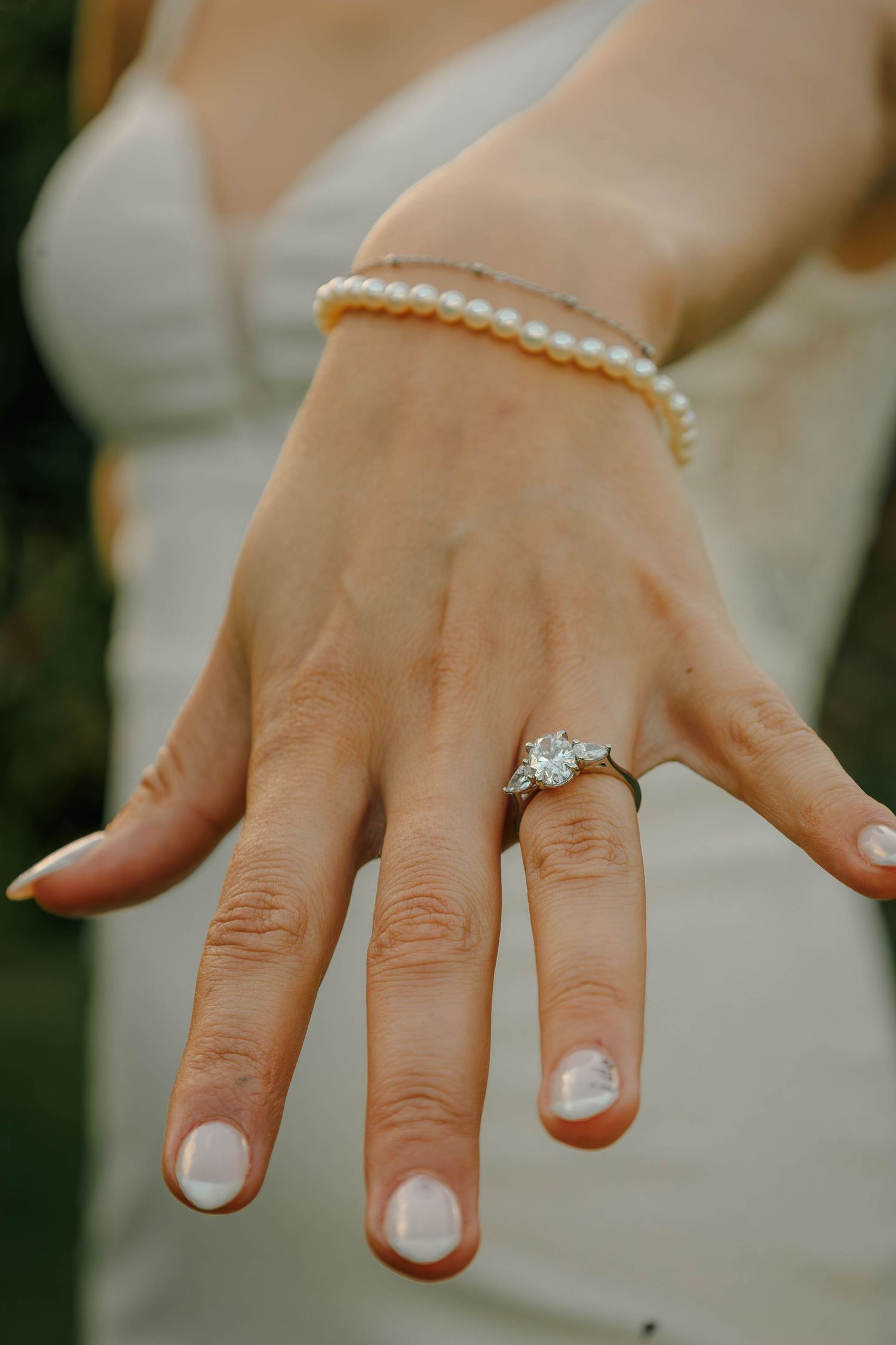 Close-up of bride's hand displaying diamond engagement ring with pearl bracelet.