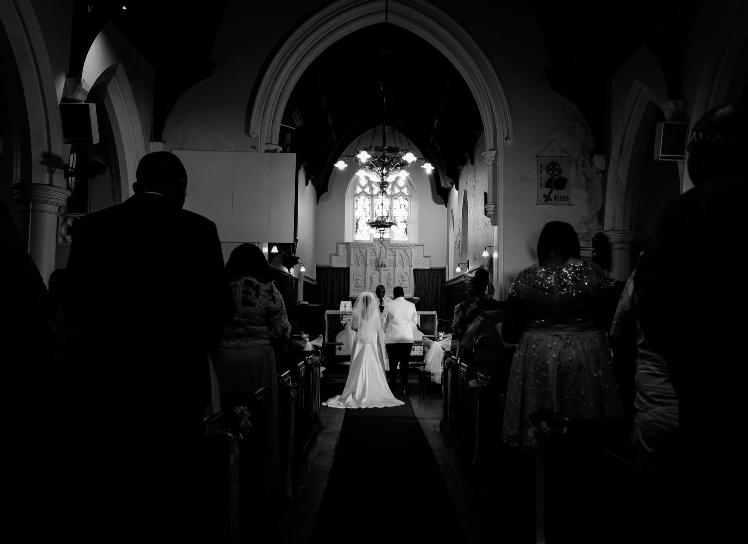 Dramatic black and white silhouette of bride and groom at candlelit church altar.