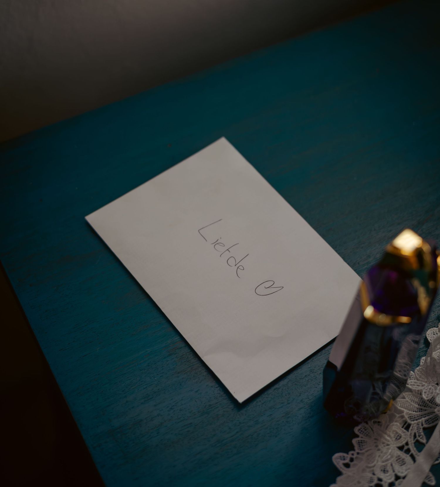 Handwritten note on white paper reading 'Liefde' with a heart, placed on a teal wooden surface.