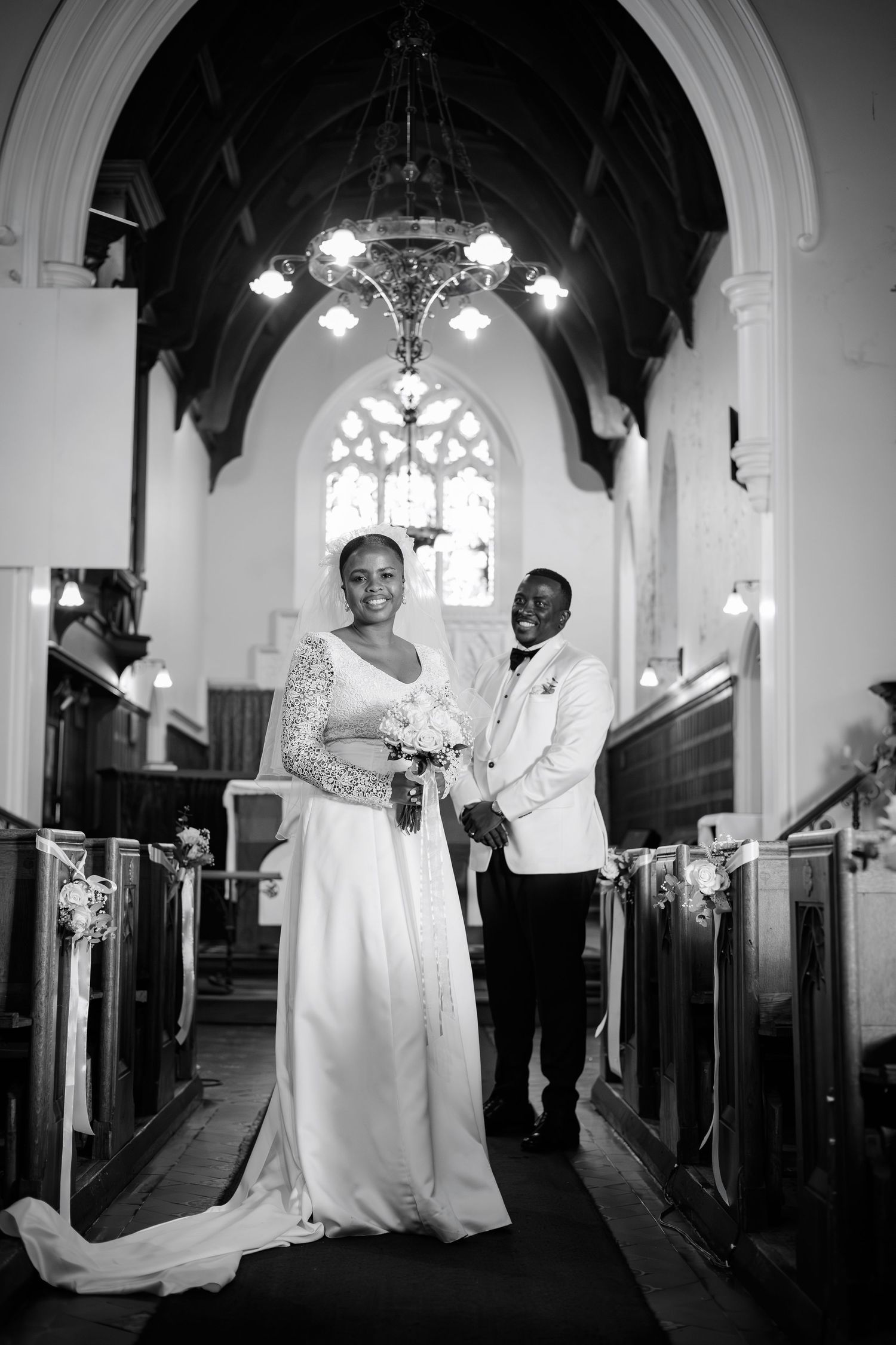 Black and white photo of a bride and groom standing elegantly in a church aisle after their ceremony.