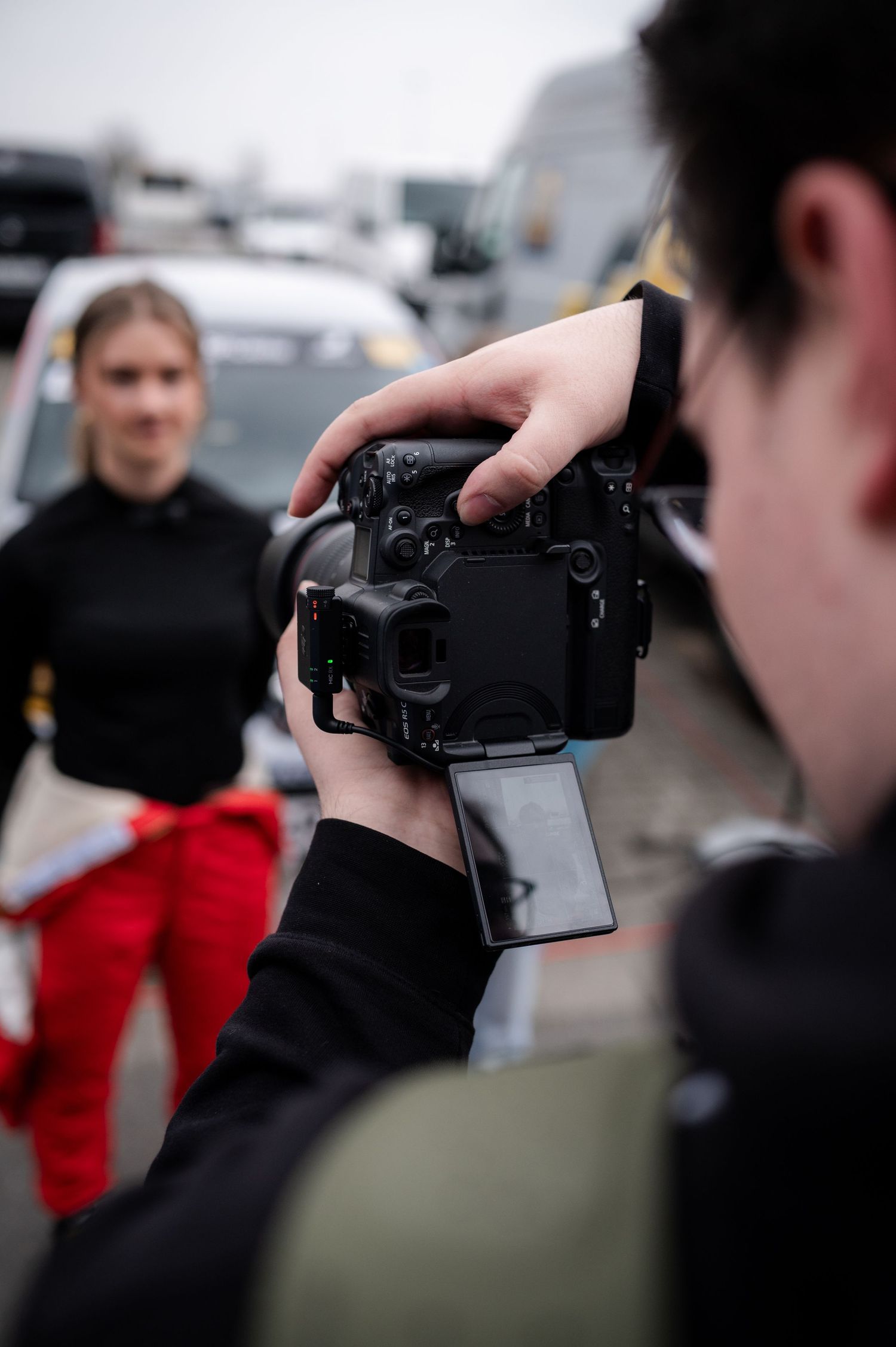 Photographer using a DSLR camera with flip screen to photograph a blonde woman outdoors at an event.