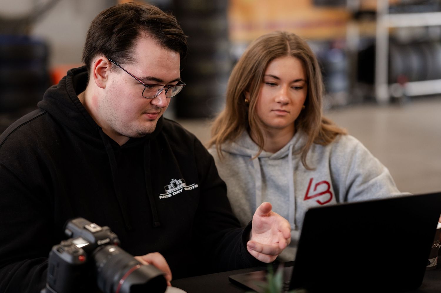 Two young professionals collaborating on a laptop computer in a modern workspace with a camera nearby.