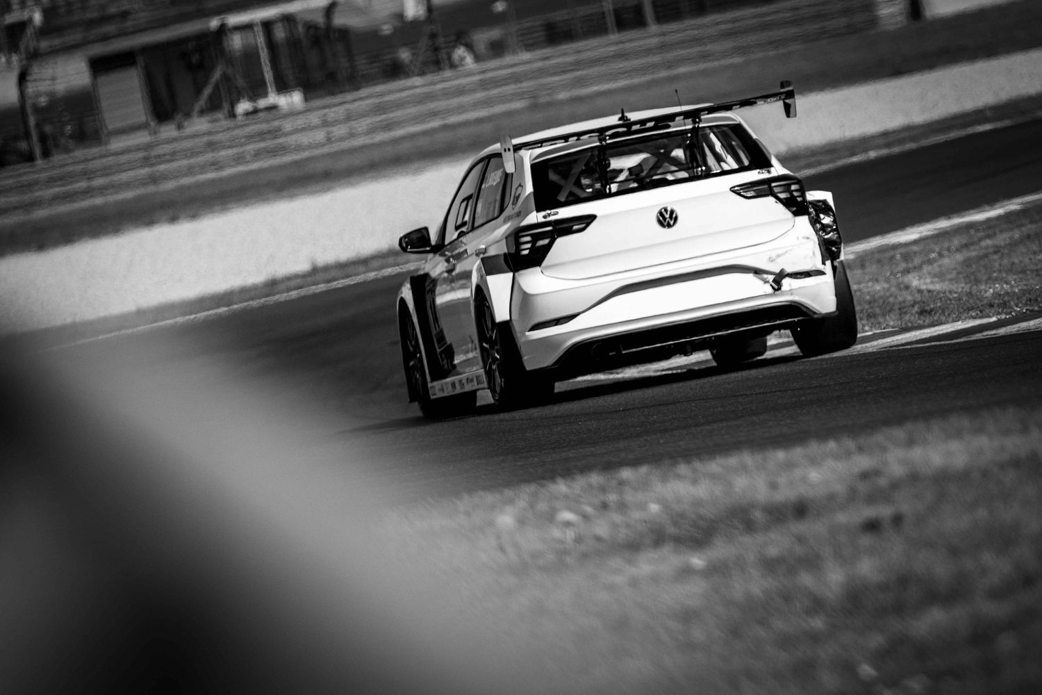 Black and white photo of a racing car on a track, captured from behind during a motorsport event.