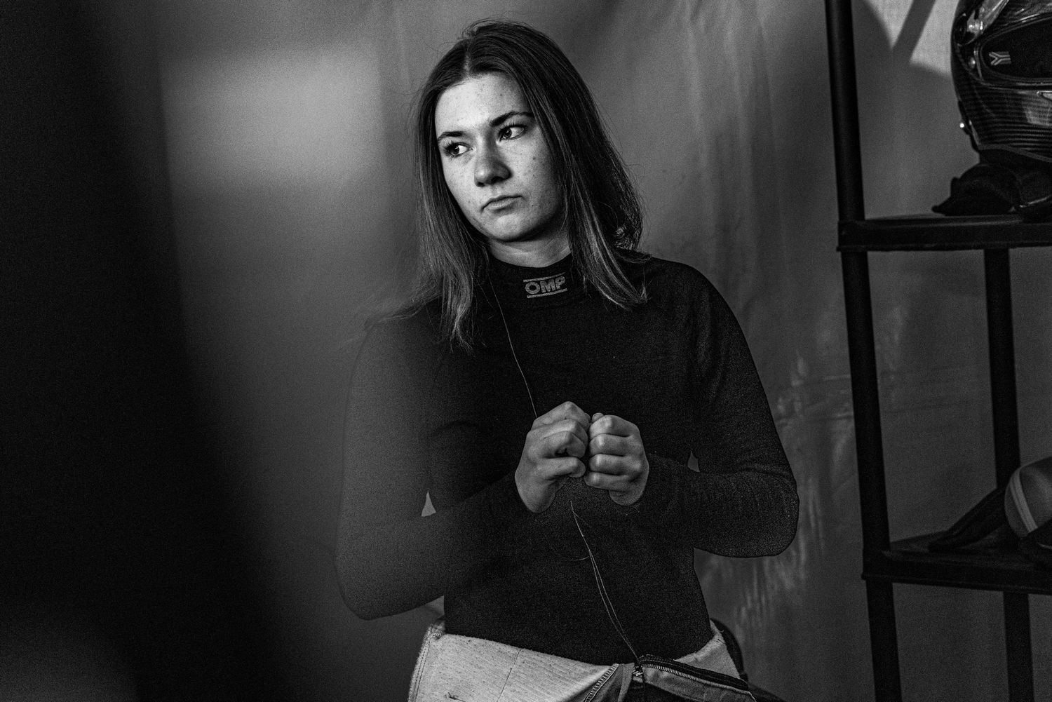 Black and white portrait of a young woman in a black turtleneck, posing with hands clasped in a studio setting.