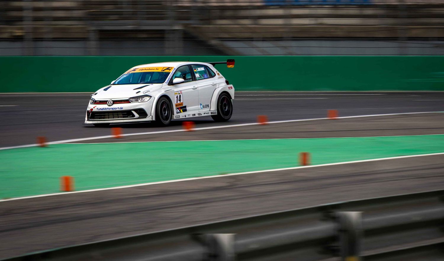 White racing car competing on a professional circuit track with green barriers and orange pylons marking the course.