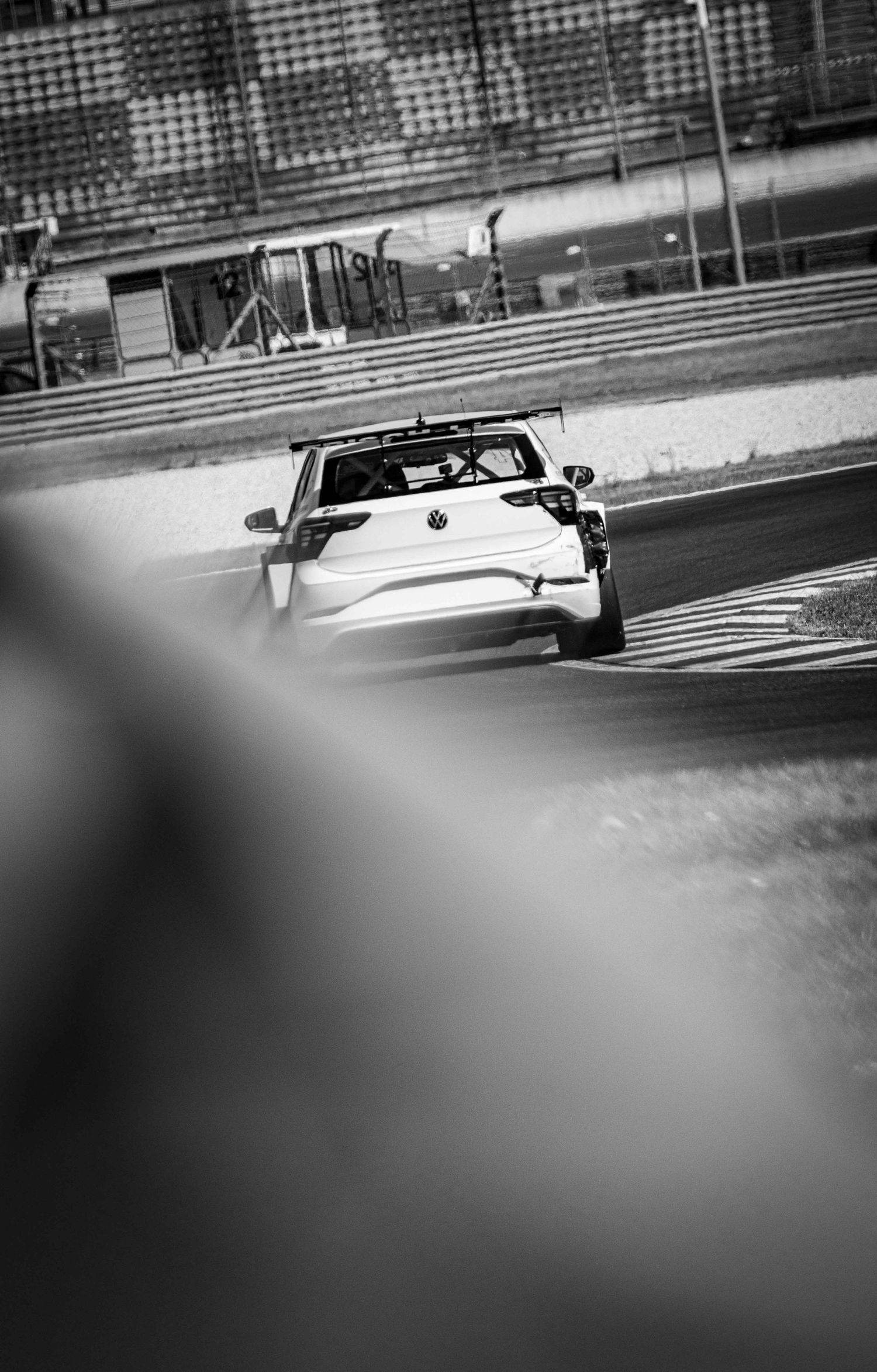 Black and white photo of a white Volkswagen race car speeding on a motorsport circuit track.