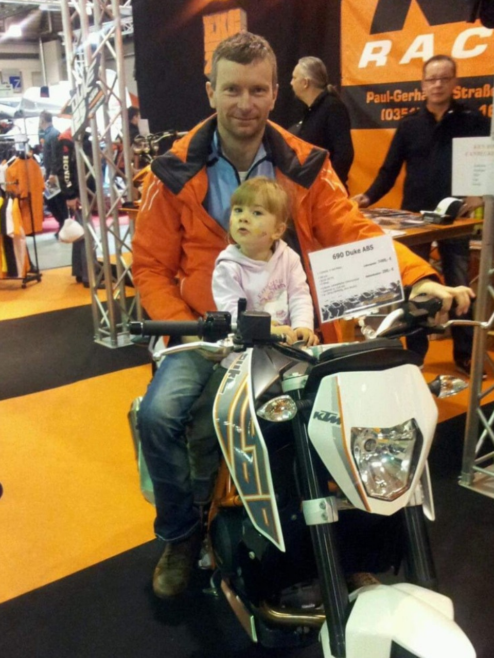 Motorsport-Messestand mit orangefarbenem Branding und Motorradausstellungen.