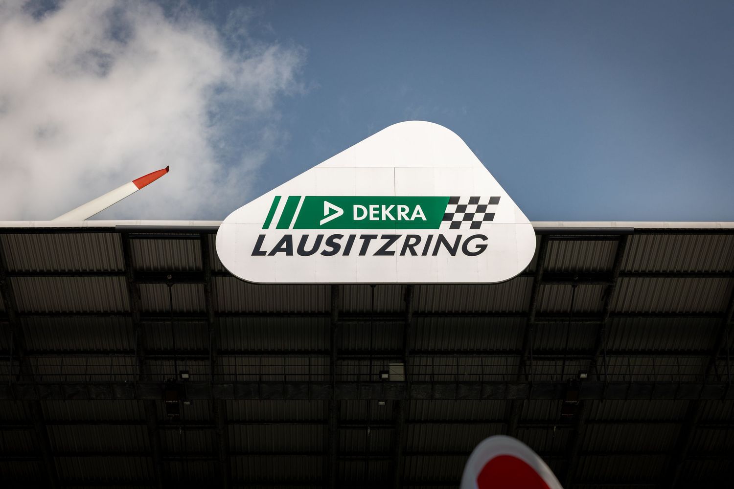 DEKRA Lausitzring motorsport circuit sign mounted on a building facade against a partly cloudy sky.