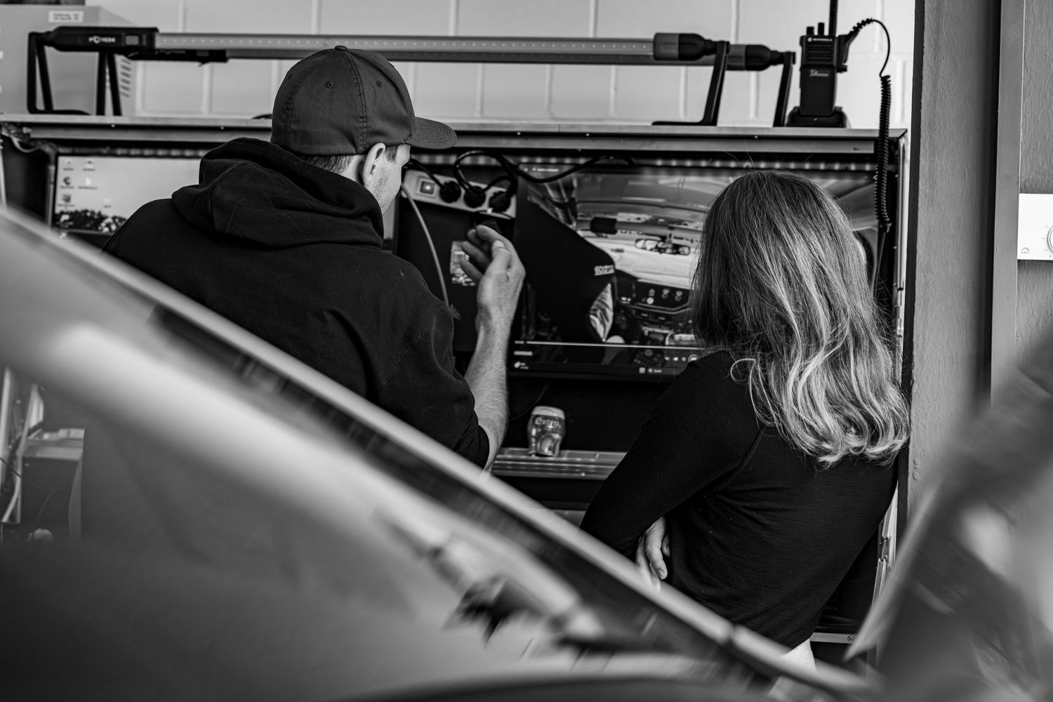 Two mechanics inspecting a car dashboard in a garage, black and white photo.