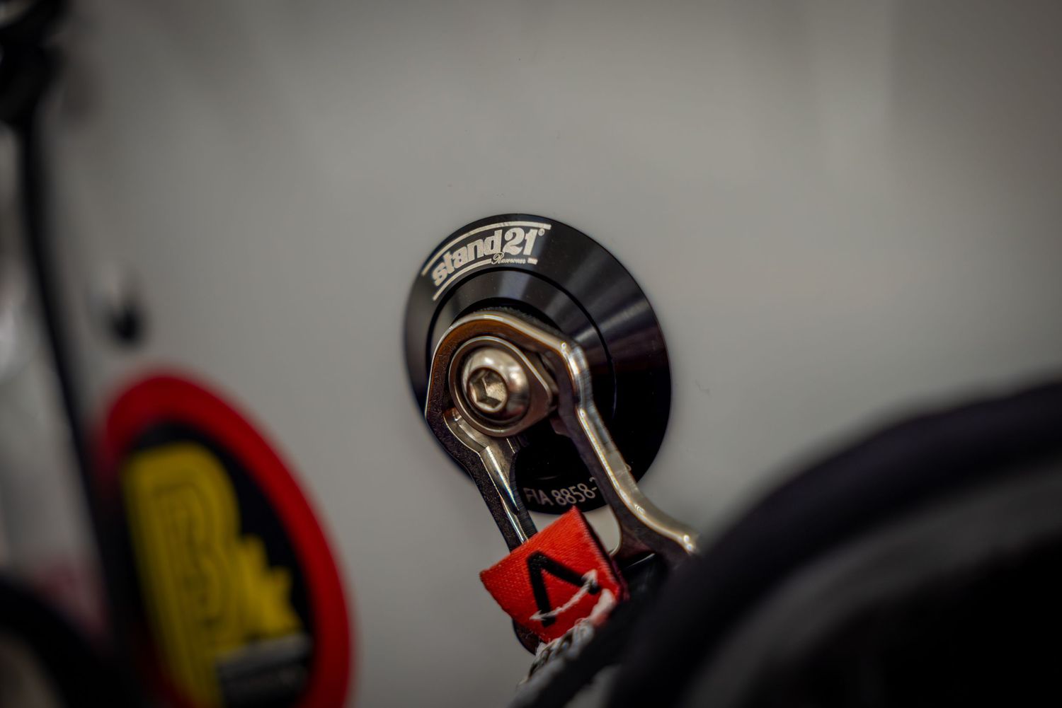 Close-up of a Sparco fuel cap with quick-release latch on a racing car, featuring red safety clip.