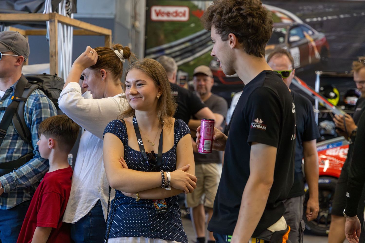 Young adults socializing at a motorsport event indoors, with racing banners visible in the background.