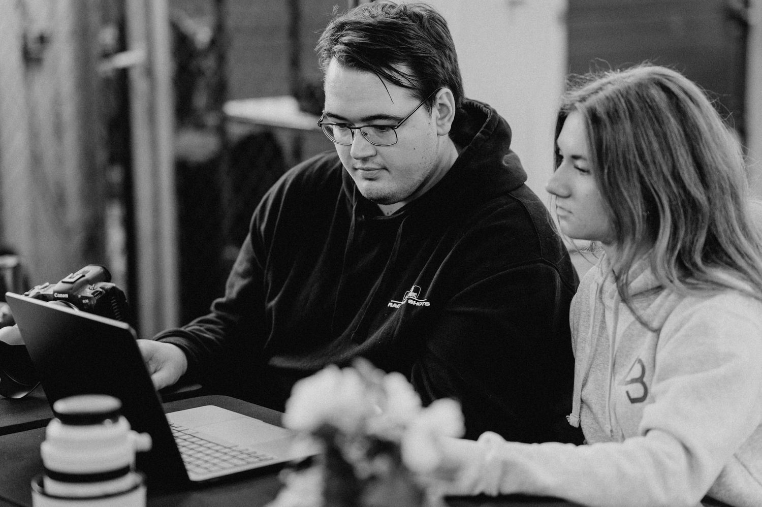 Two colleagues collaborating on a laptop at a desk in a modern workspace, black and white photo.