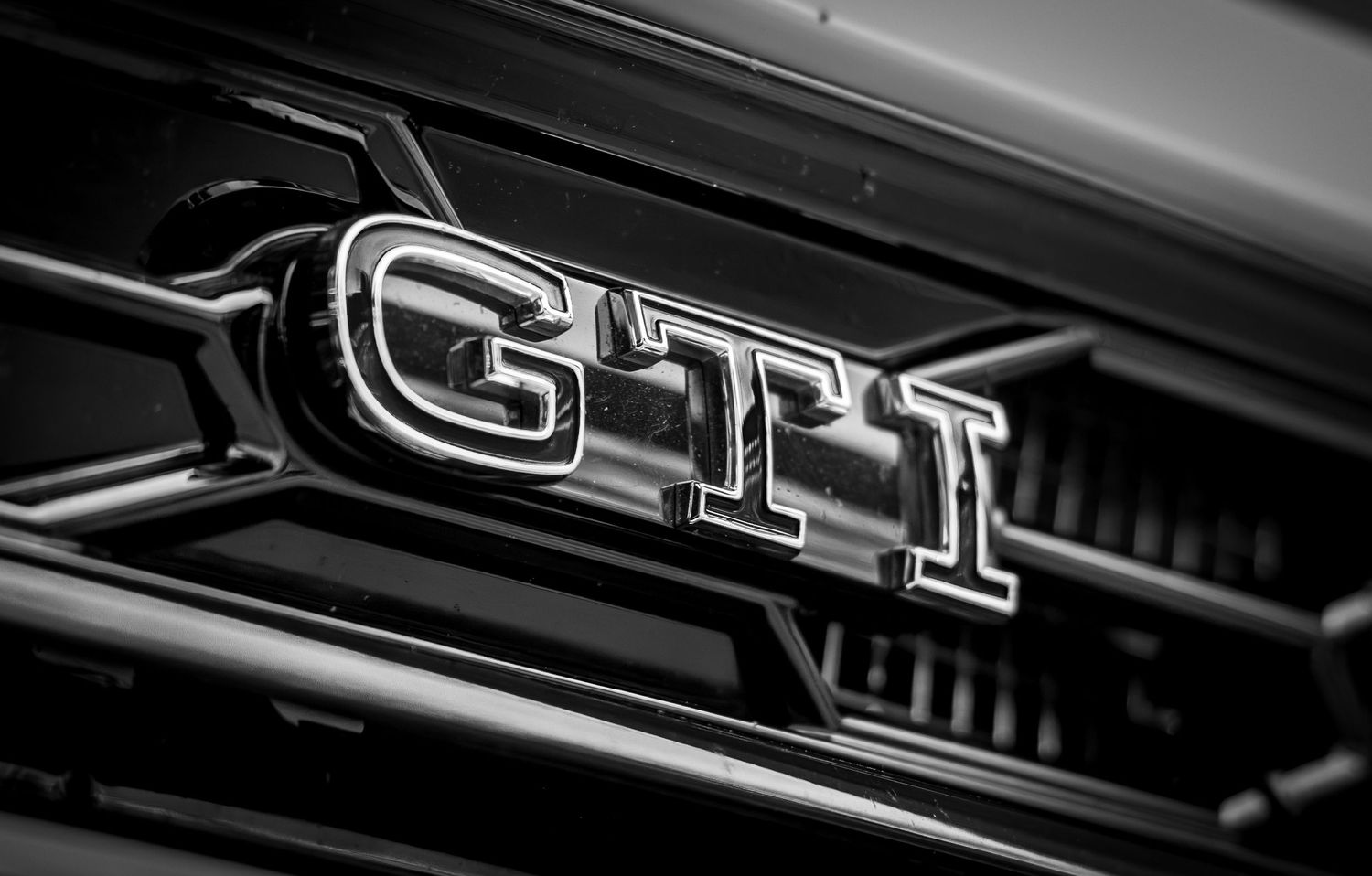 Close-up black and white photo of a Volkswagen GTI chrome badge on a car grille.