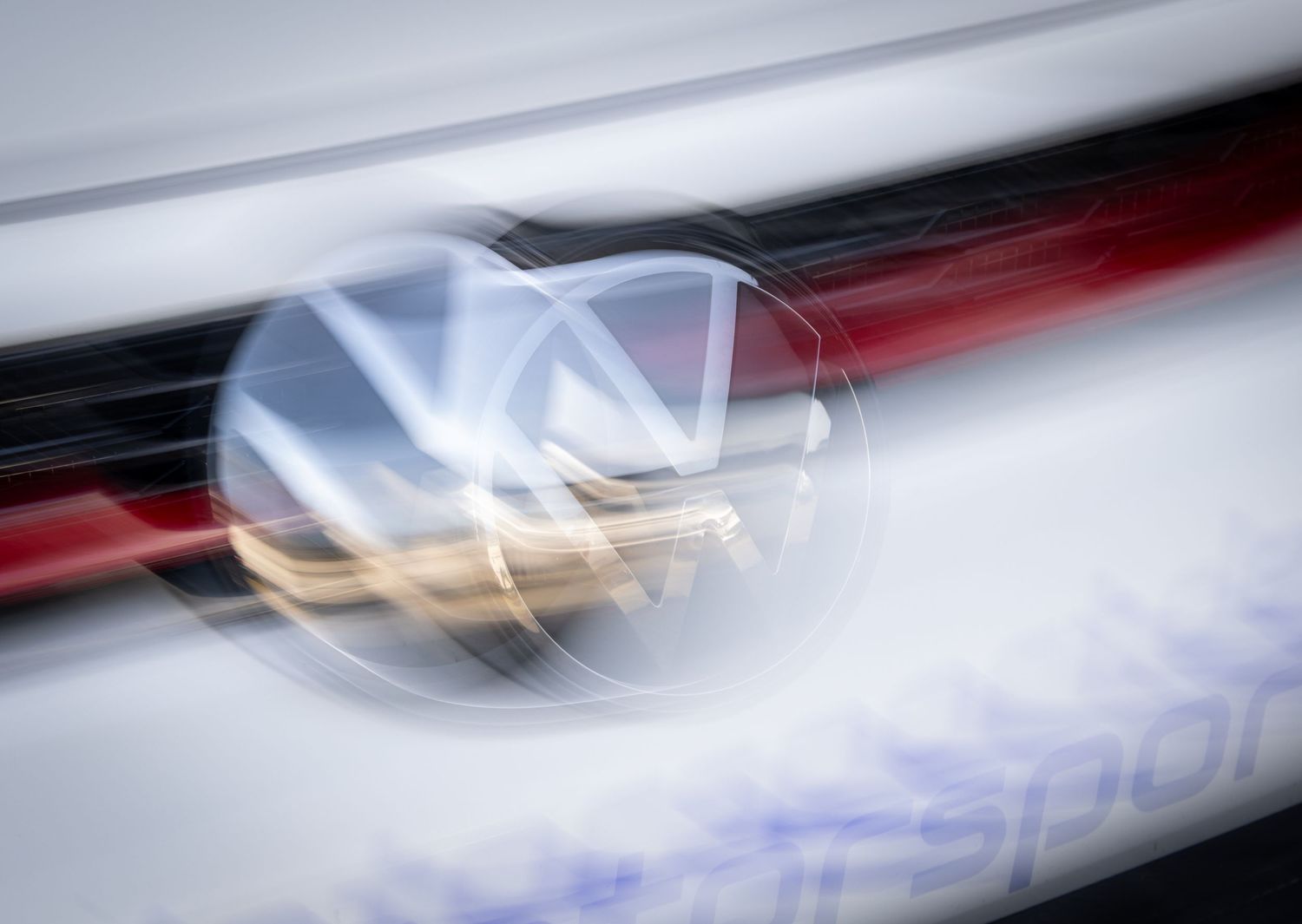 Blurred motion shot of a Volkswagen VW logo emblem on a car, with red and white streaks suggesting high speed.