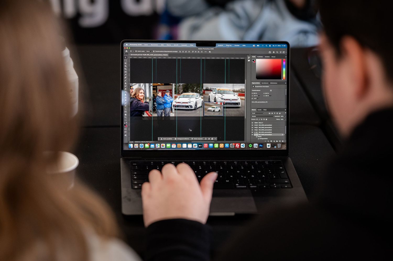 Two people editing car racing footage in Adobe Premiere Pro on a MacBook laptop in a dark studio.