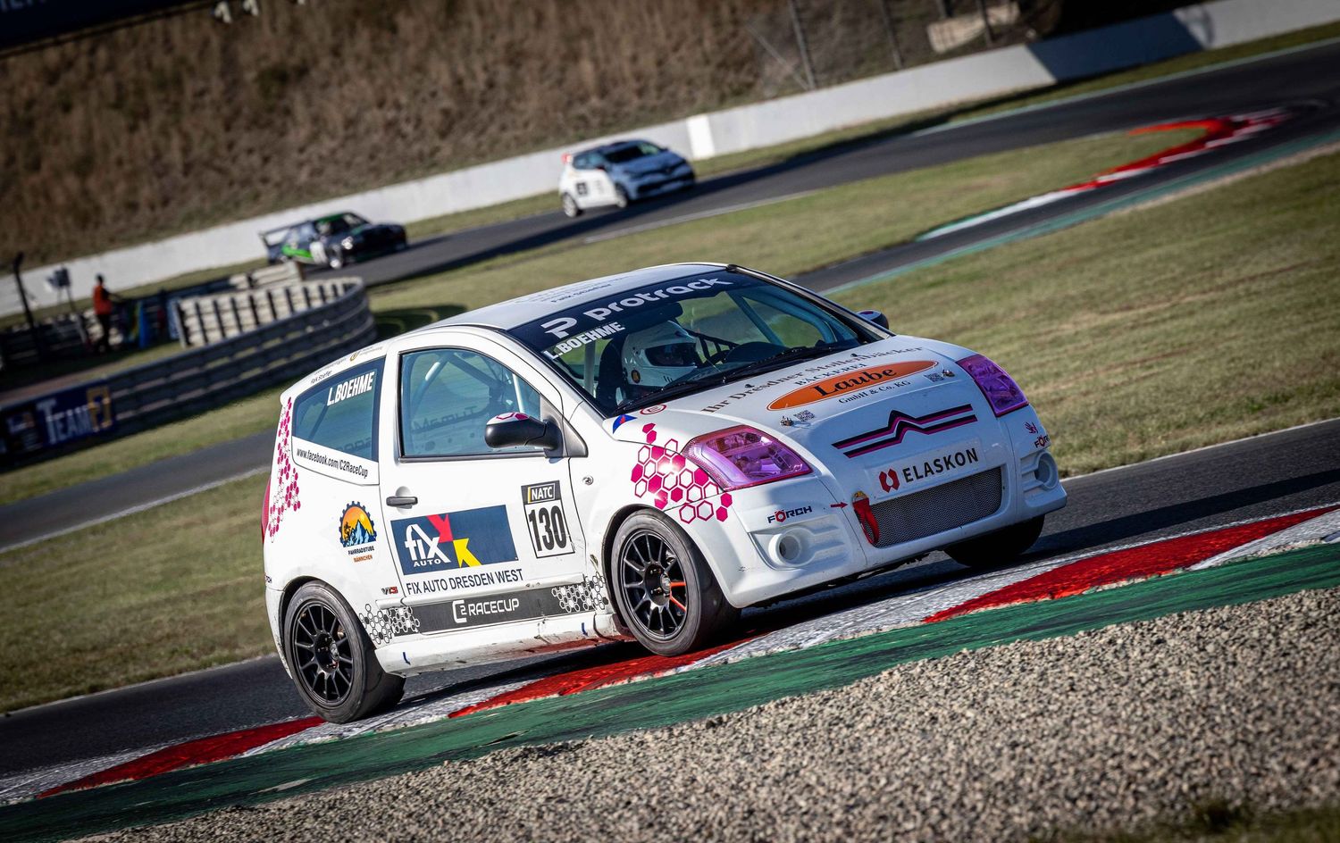 White race cars line up on a racing circuit with grass and gravel runoff areas.