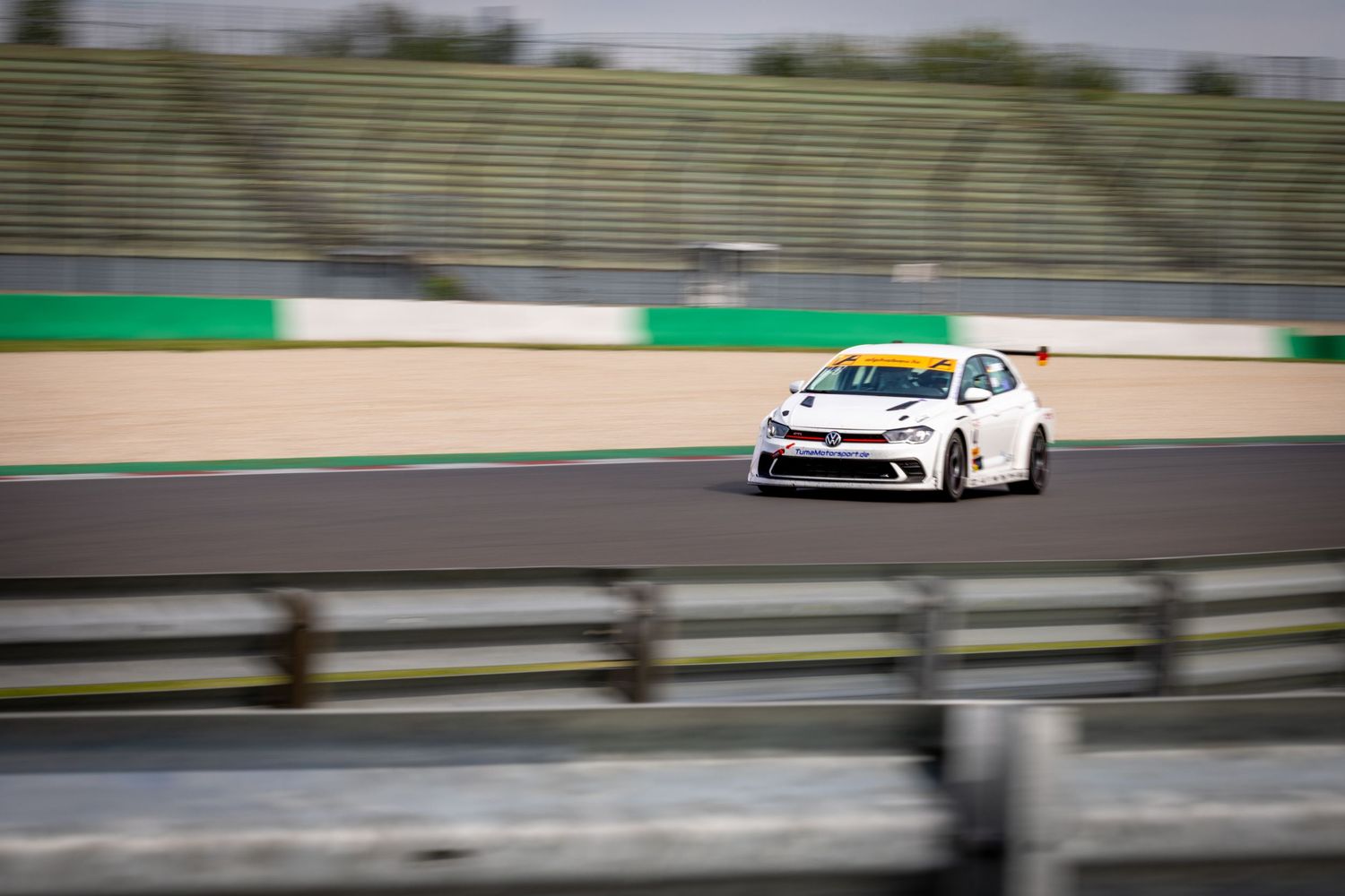 White racing car speeding on a professional circuit track during a motorsport event on a cloudy day.
