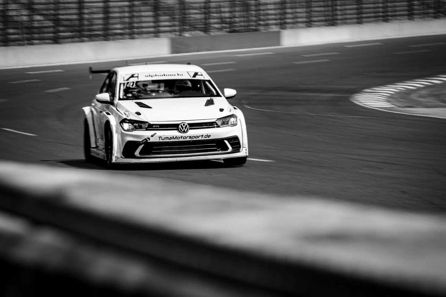 Black and white photo of a Volkswagen race car speeding around a track corner during a motorsport competition.