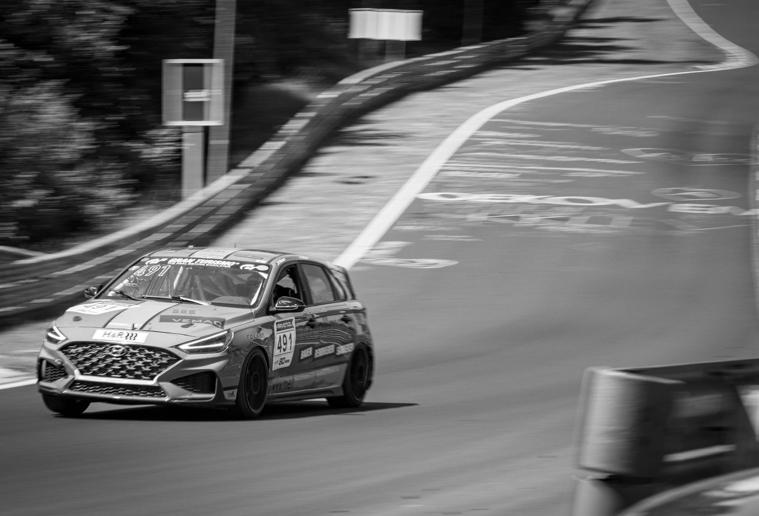A racing Hyundai i30 N navigates a curve on a race track in black and white photography.