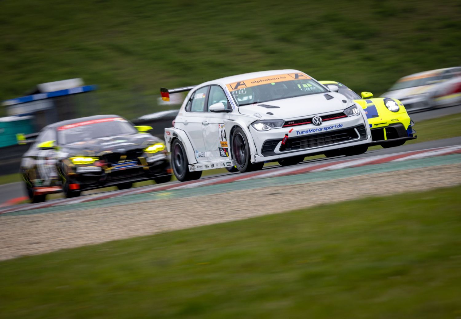 White VW racing car leads competitors on a wet circuit during a professional touring car championship race.