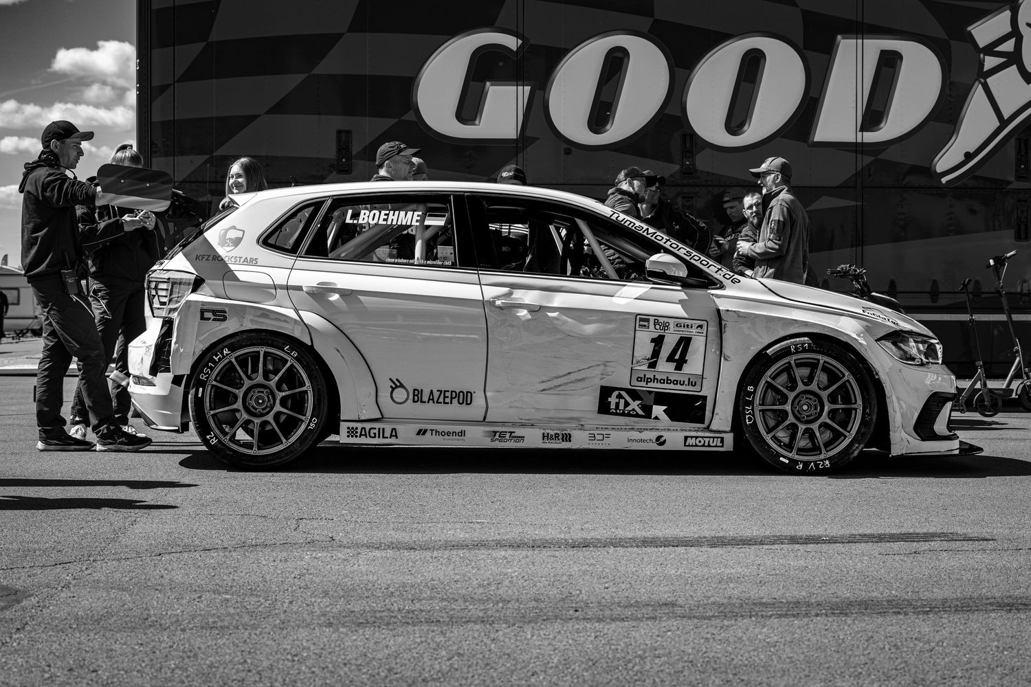 Black and white photo of race car #14 in pit lane with crew members, Goodyear signage visible in background.
