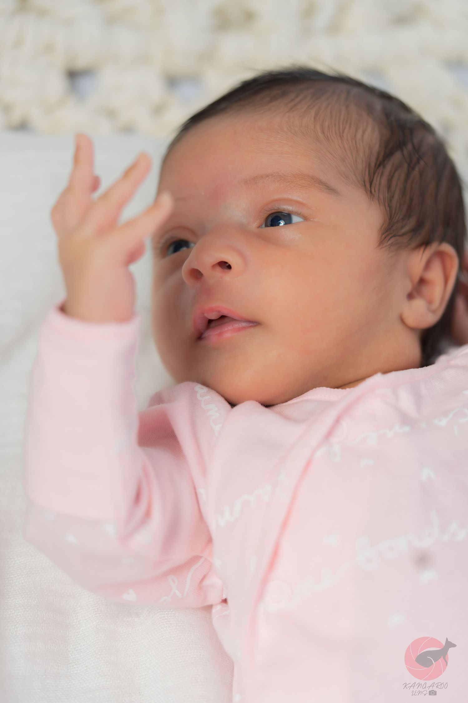 Close-up portrait of infant in soft pink clothing against white background.