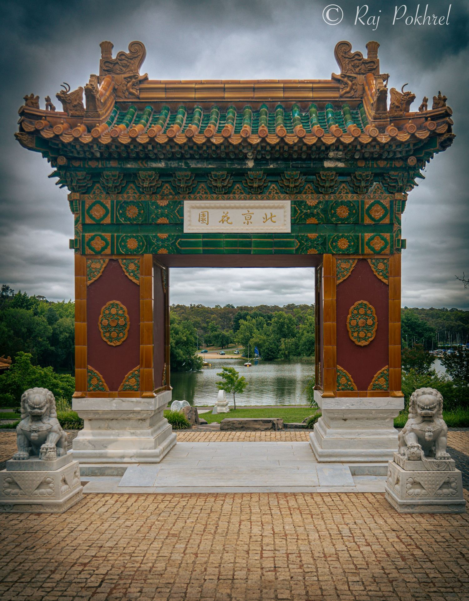 Traditional Chinese gateway with ornate decorations and guardian lions under moody sky.